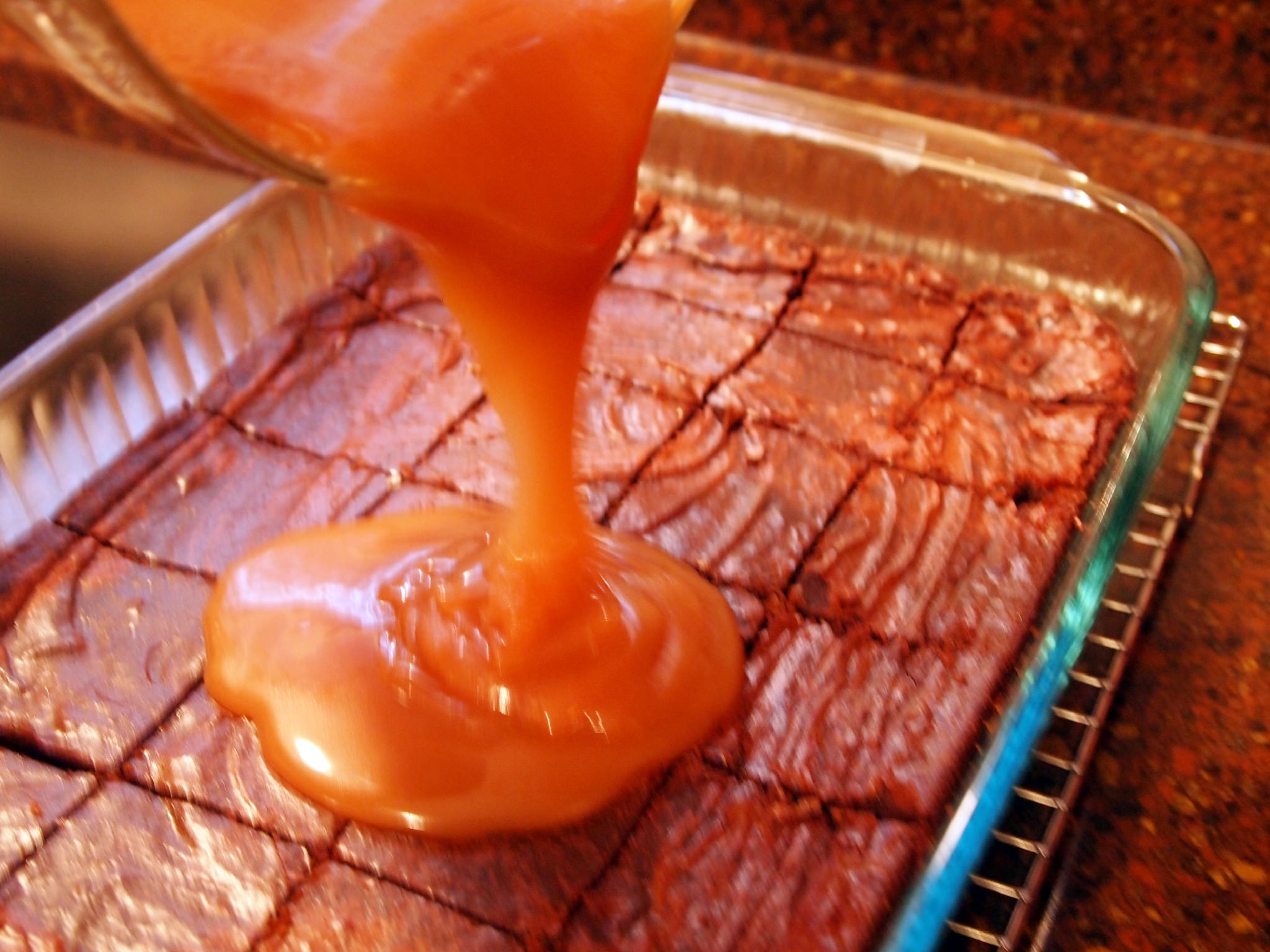 pouring salted caramel onto a pan of brownies
