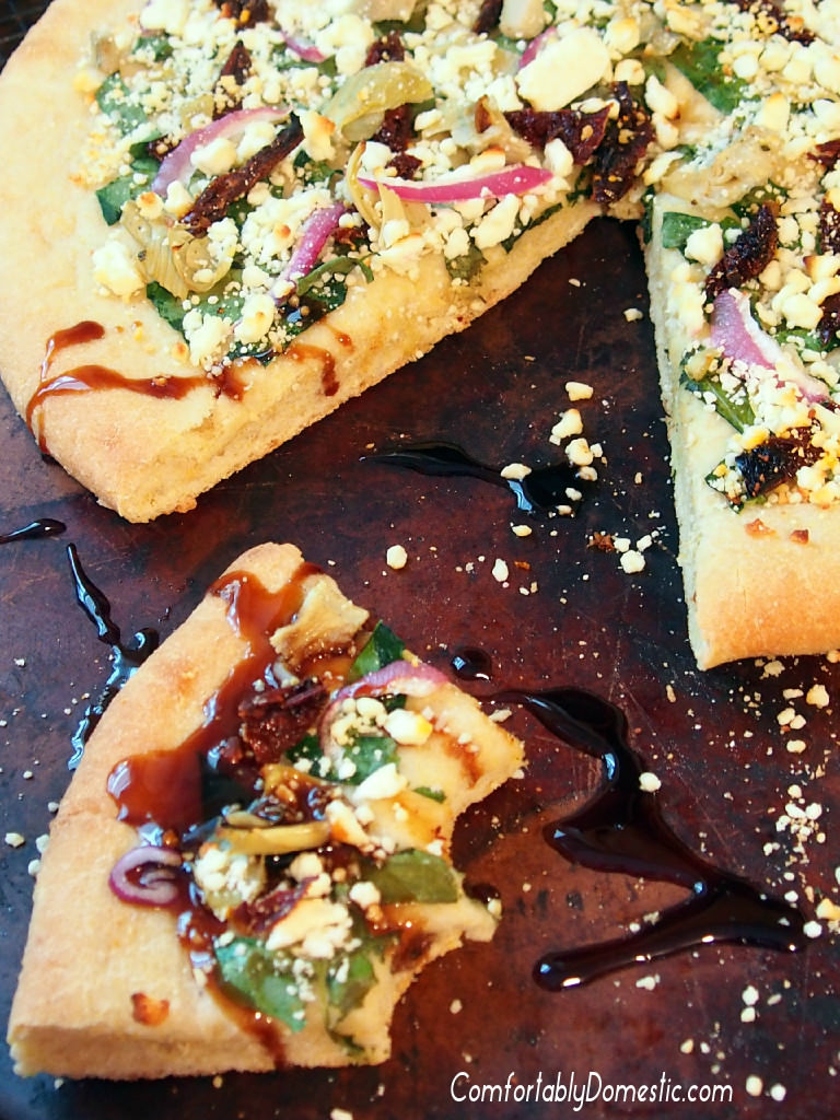 Greek Pizza-with-Balsamic-Glaze starts with a tangy tzatziki sauce that unites such Mediterranean flavors as artichoke hearts, sundried tomatoes, spinach, red onion, and a feta cheese into tantalizing, cornmeal-crusted pizza. | ComfortablyDomestic.com
