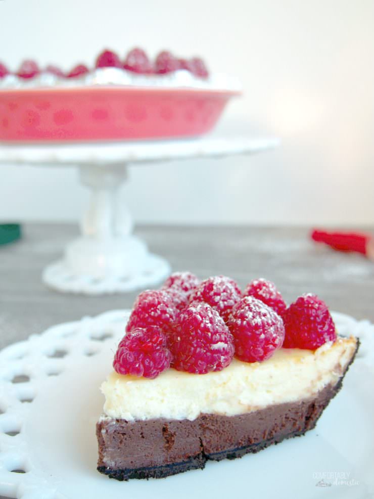 Chocolate-Layer-Cheesecake has a rich layer of vanilla cheesecake resting atop a decadent layer of chocolate cheesecake nestled in a chocolate cookie crust. Topped with fresh raspberries and whipped cream, this cheesecake is a showstopper!