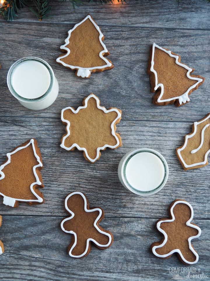 gingerbread cut out cookies scattered on a dark background with two glasses of milk.