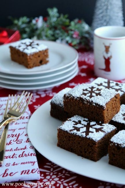 Plate of stacked gingerbread cake squares with stenciled powdered sugar snowflakes on top.