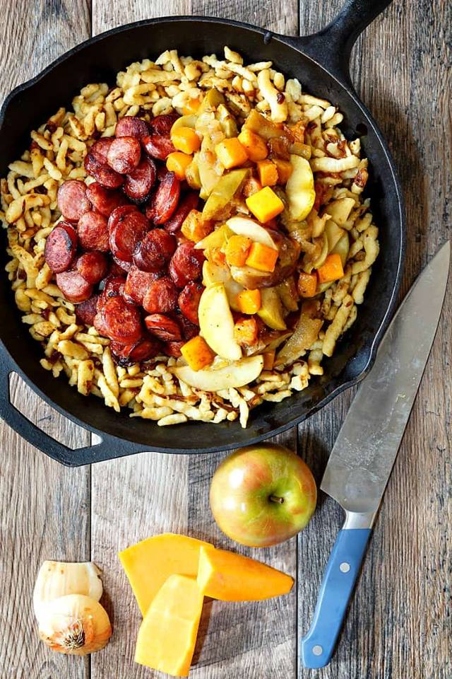 A cast iron skillet with spaetzle dumplings, sliced sausage, diced apples, and cubes of butternut squash.
