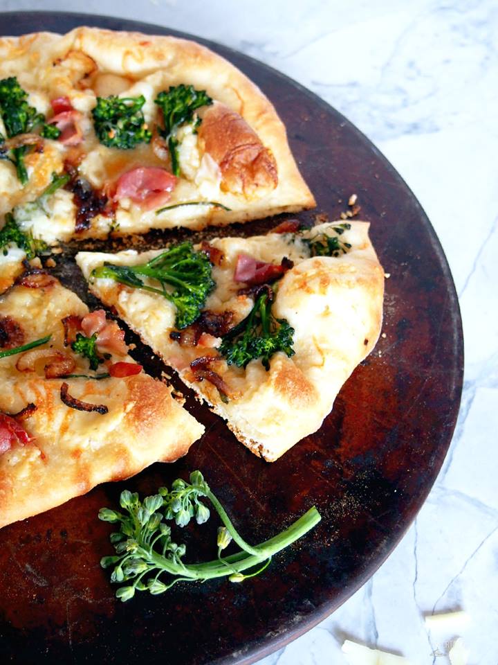 Crisp pizza with broccolini, prosciutto, and shaved parmesan cheese on a dark pizza stone. 