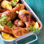 baked chicken drumsticks in a stainless steel roasting pan on blue background