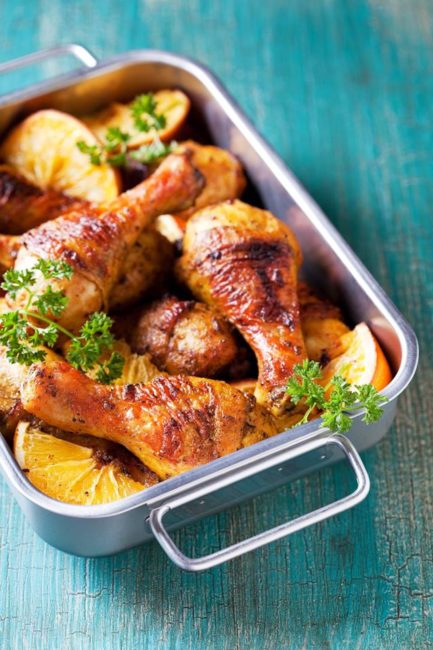 baked chicken drumsticks in a stainless steel roasting pan on blue background