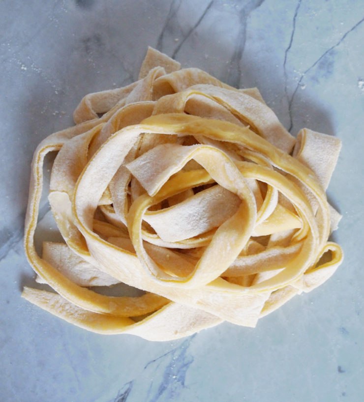 homemade egg noodles spun into a nest like pile on white marble.