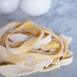 a pile of homemade egg noodles on white marble with two eggs in the background.