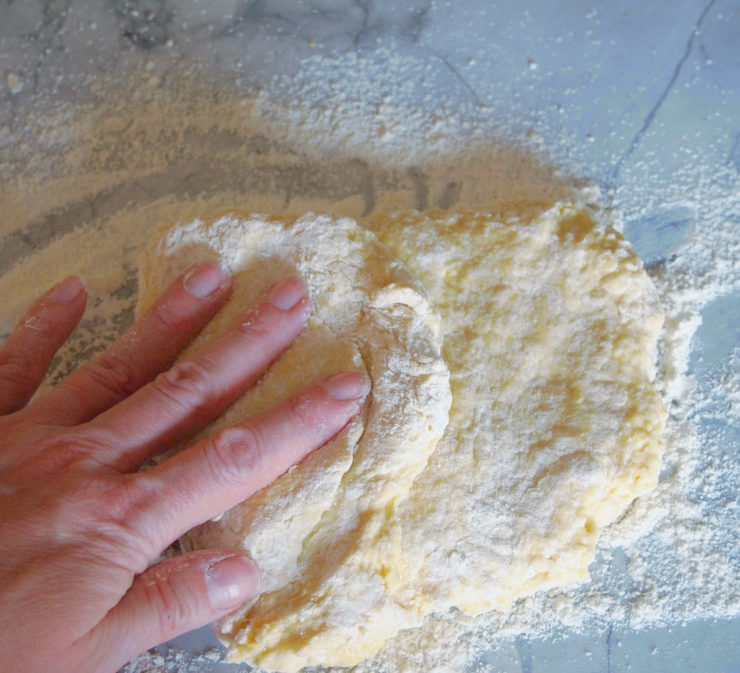 hand kneading egg noodle dough on a white marble surface.