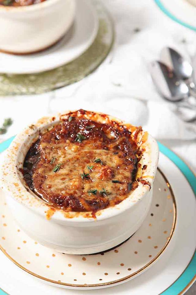White crock full of french onion soup with melted cheese on top.