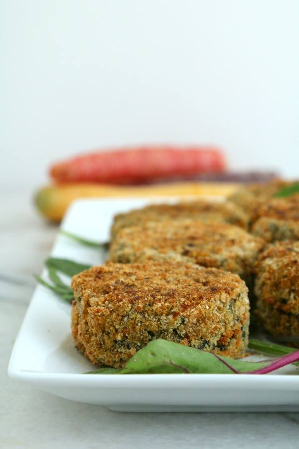 Close up photo of vegetable cakes coated in breadcrumbs on a white plate. 