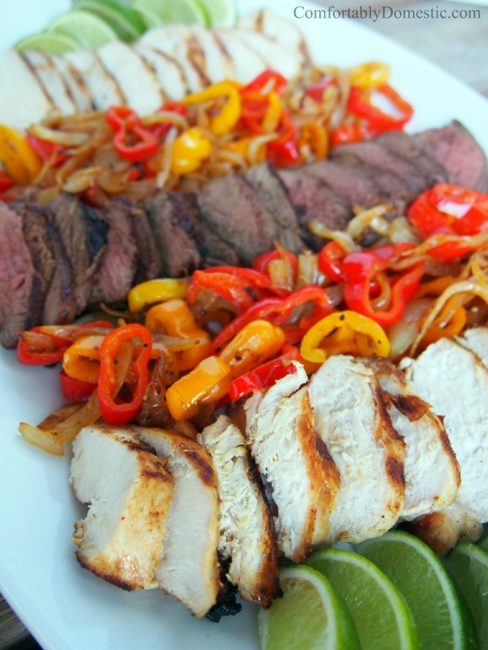 sliced steak and chicken on a white platter with lime wedges and roasted sweet peppers and onions.