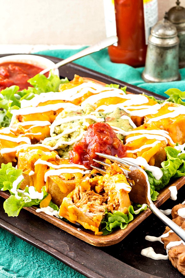crispy-flauta-bites on a wood platter with lettuce, salsa, and a drizzle of sour cream