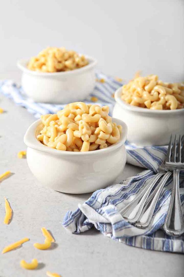 three white bowls of instant pot macaroni and cheese with a blue pinstripped napkin.