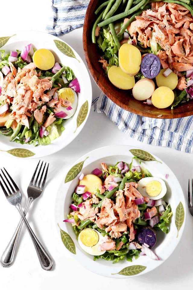 three bowls of salmon niscoise salad in white bowls with a blue striped napkin
