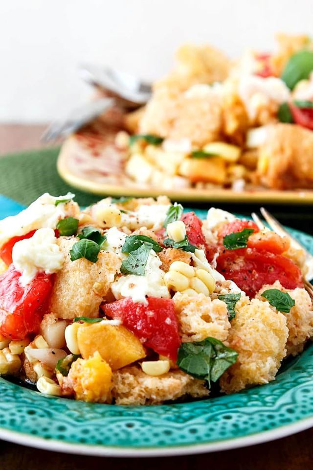 heaping bowl of tomato peach panzanella on a teal plate.