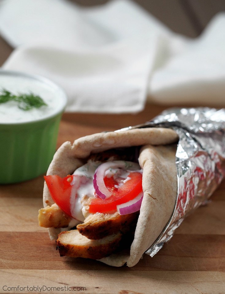 grilled chicken gyro rolled in a pita with tomato, onion, and tzatziki sauce on a cutting board.