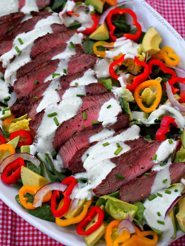 sliced grilled steak on a bed of mixed greens with colorful sweet peppers and drizzled with yogurt dressing. 