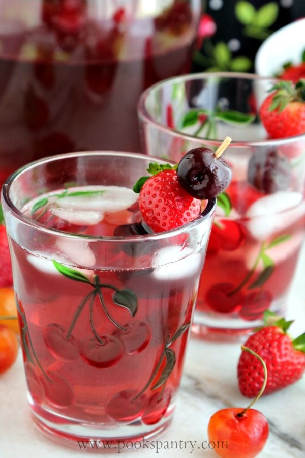 glass of strawberry and cherry wine spritzer garnished with sweet cherries and strawberries.