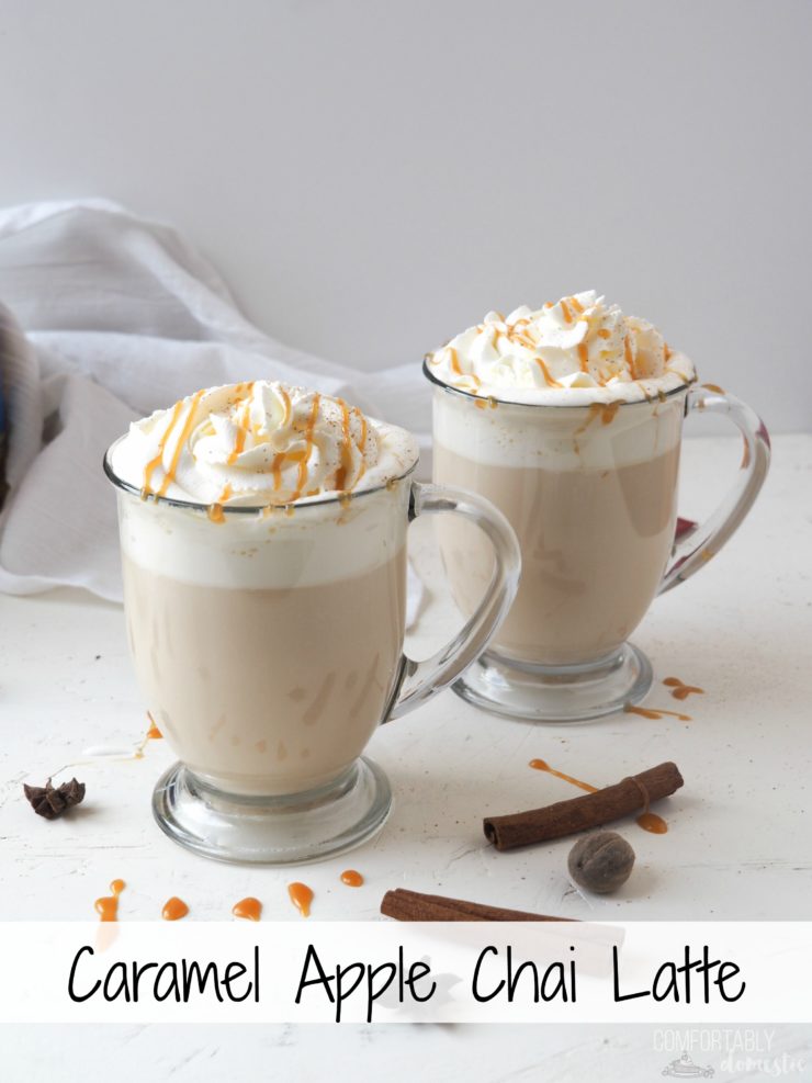 Two glass mugs of caramel apple chai latte with whipped cream, grated nutmeg, and caramel on top. 