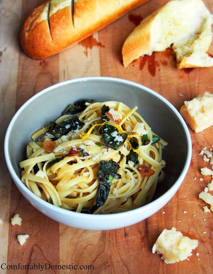 white-bowl-of-lemon-garlic-linguine-with-fresh-kale on a cutting board with a baguette and crumbled parmesan