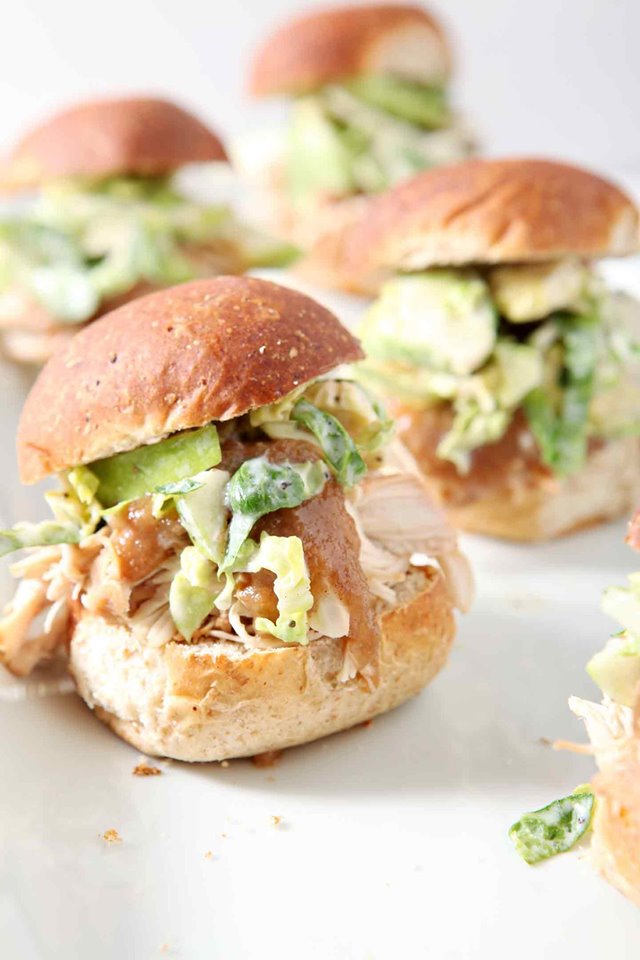 Several apple pulled chicken sliders on buns on a white platter.