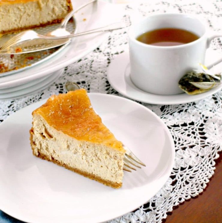 slice of cinnamon cheesecake on a white plate with a cup of tea.