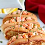 White platter of lobster rolls with warm butter being poured over top.