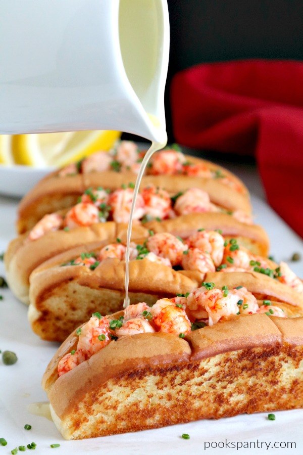 White platter of lobster rolls with warm butter being poured over top. 