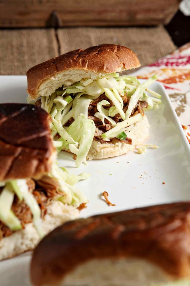 several apple-cider-pulled-pork-sandwiches with cabbage slaw on a square white plate.