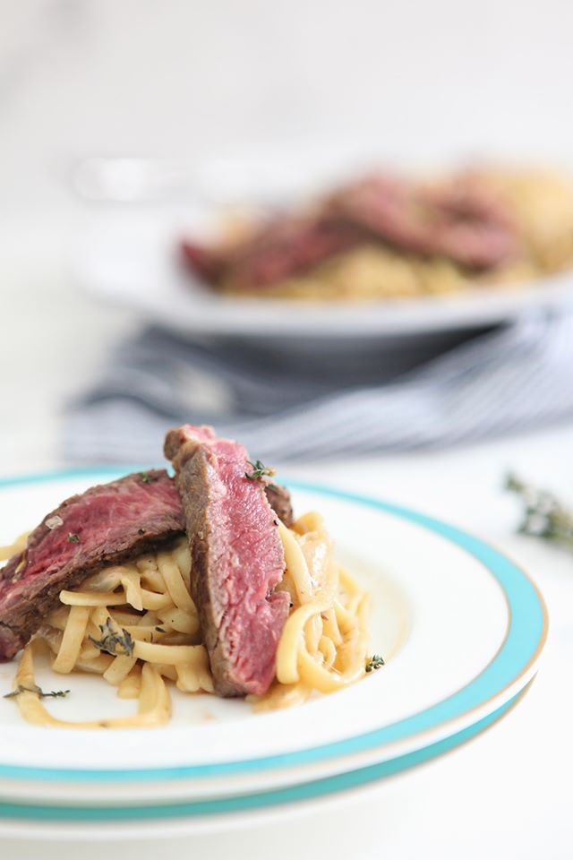 Large white plate of french onion pasta with sliced steak on top.