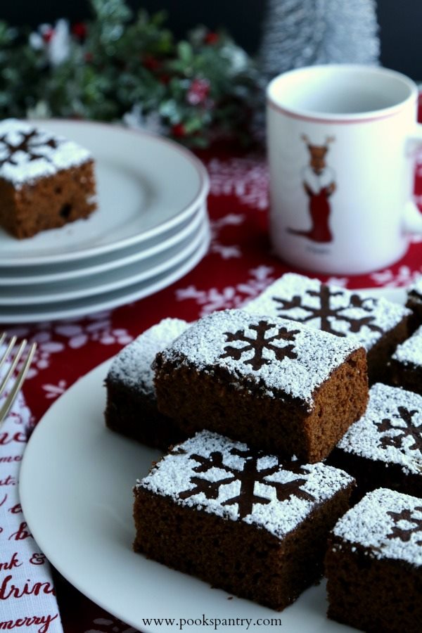 A white plate piled high with slices of gingerbread cake with powdered sugar snowflakes on top.