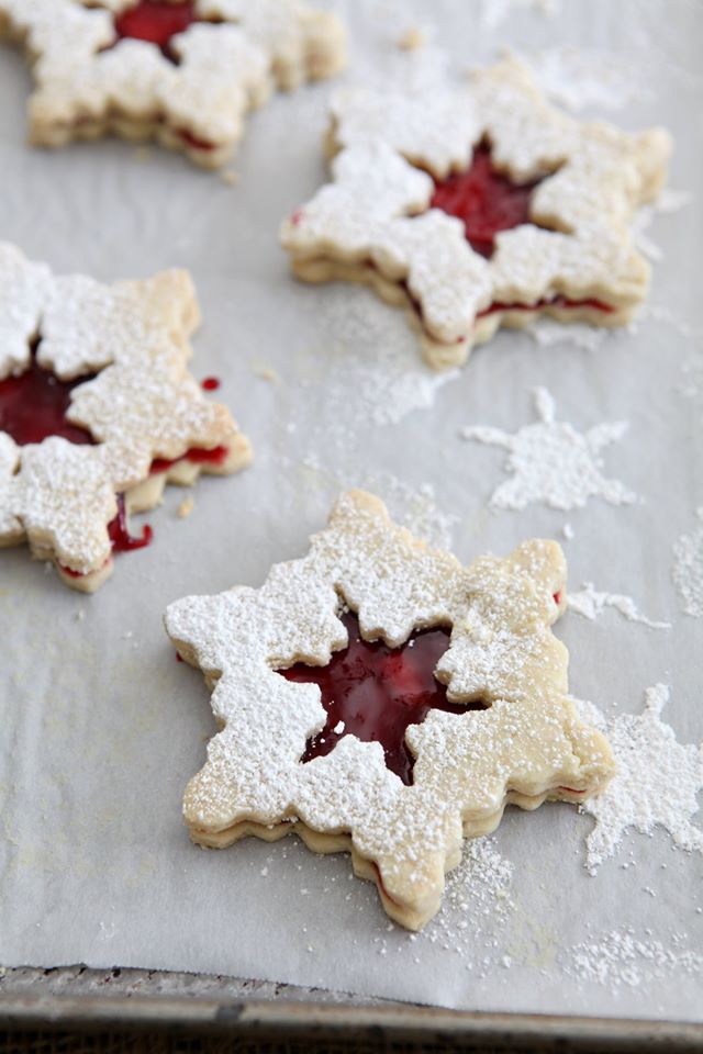 A trio of raspberry linzer snowflake cookies on parchment paper. 