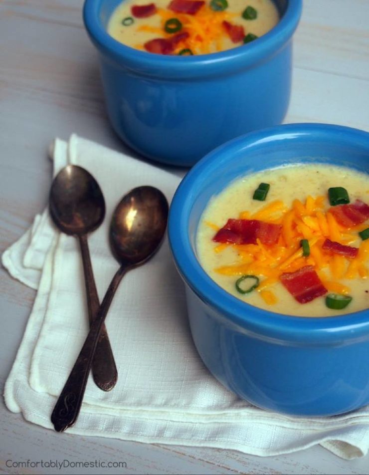 Luscious lighter loaded baked potato soup in blue bowls with spoons on the side. 