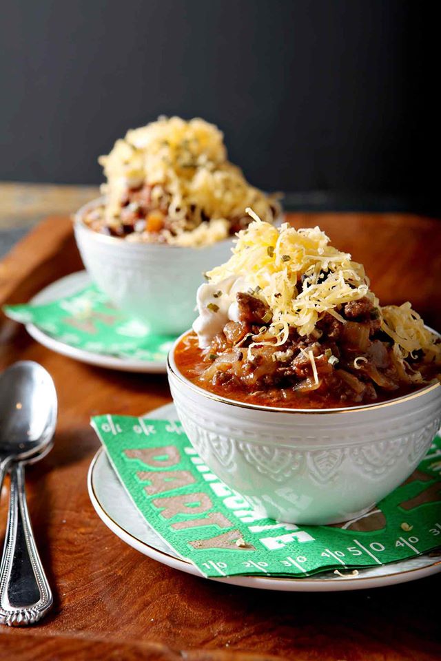 Two white bowls heaping with shiner bock flavored chili and cheese. 