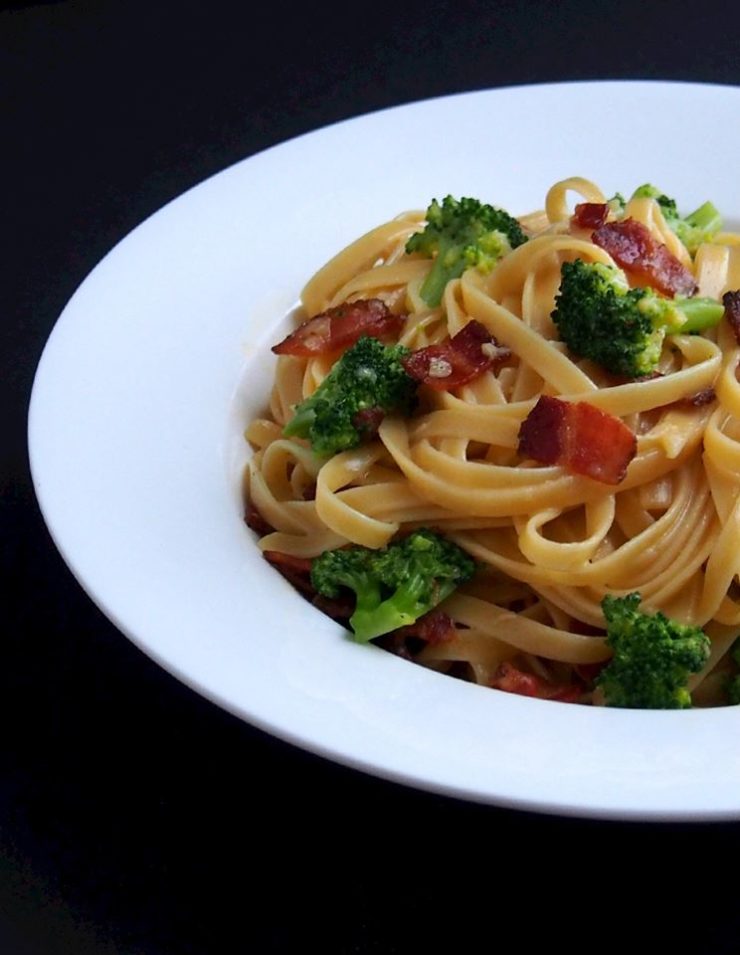 Heaping bowl of Broccoli bacon Carbonara pasta in a white rimmed bowl. 