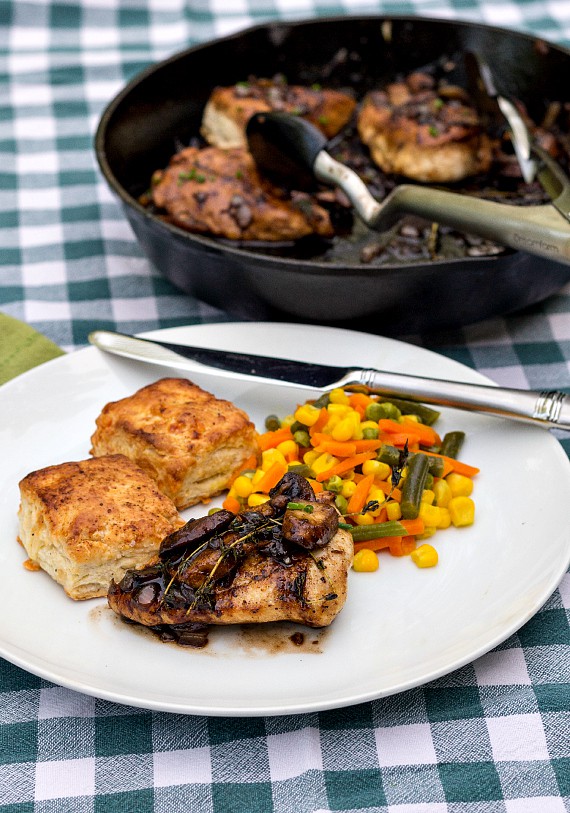 Chicken-with-mushrooms and thyme served with biscuits and mixed vegetables on a white plate on a blue gingham background. 