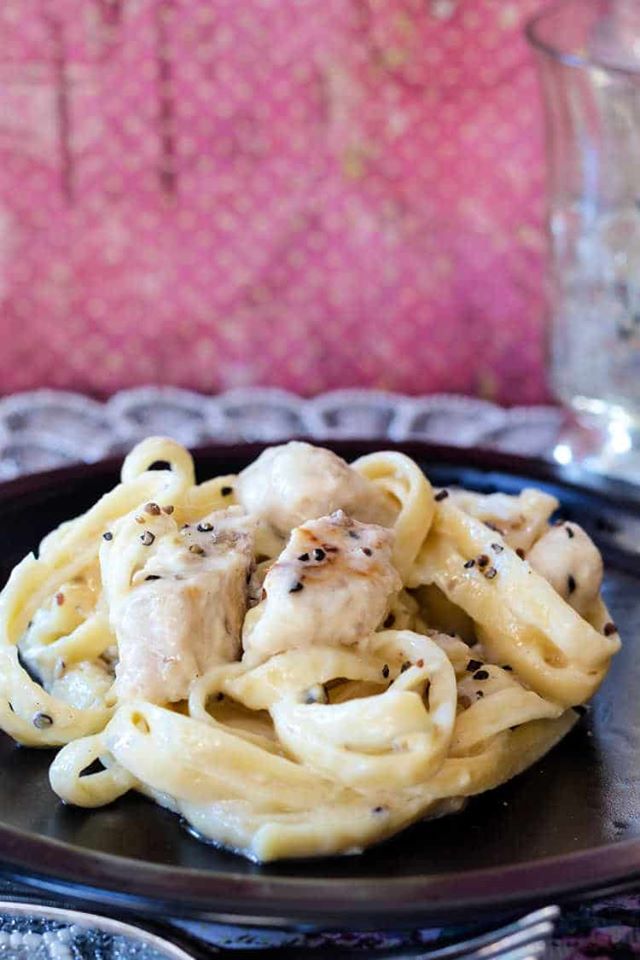 Delicate spiral of creamy pasta with chicken on a black plate.
