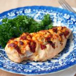 Hasselback-Stuffed-Chicken filled with cheese, artichoke hearts, and sundried tomatoes on a blue and white plate.