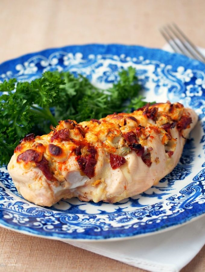 Hasselback-Stuffed-Chicken filled with cheese, artichoke hearts, and sundried tomatoes on a blue and white plate.