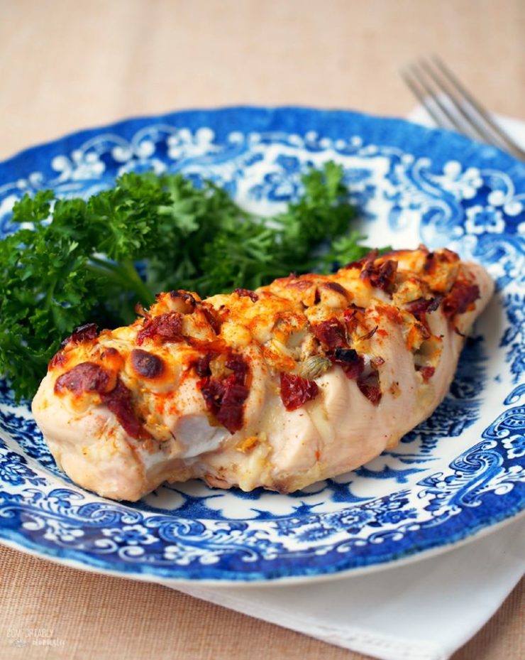 Hasselback-Stuffed-Chicken filled with cheese, artichoke hearts, and sundried tomatoes on a blue and white plate. 