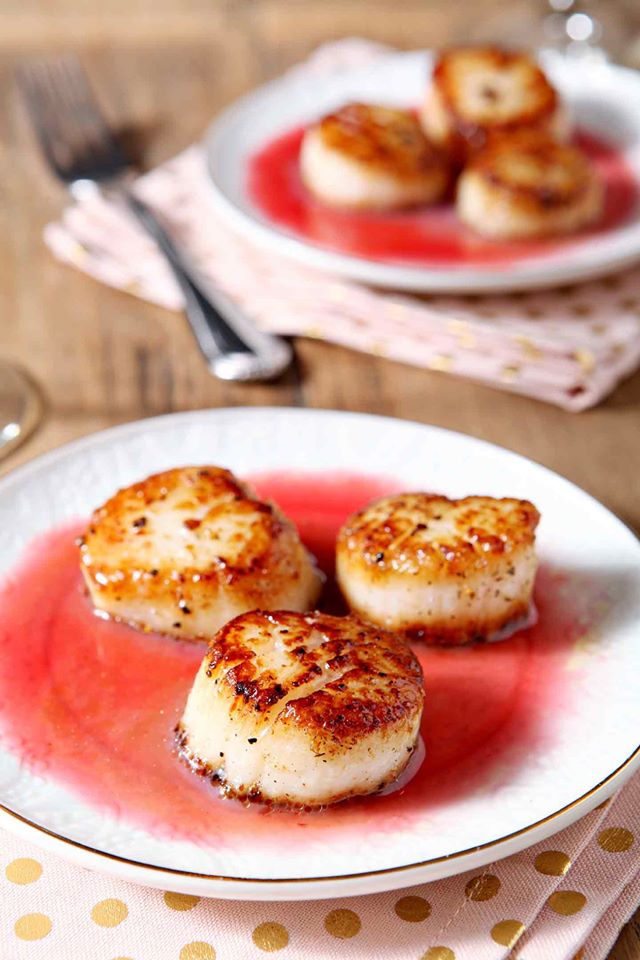 Seared-scallops swimming in raspberry gastrique on a white plate. 