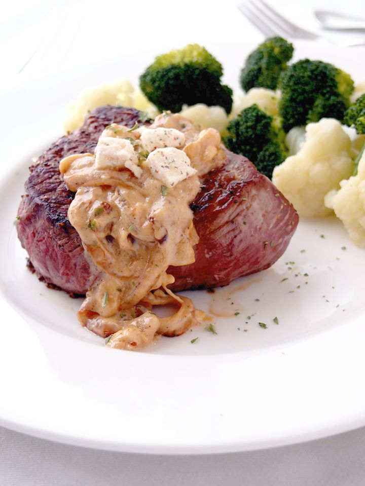 Tender sirloin steaks with creamy onion sauce with feta on a white plate.