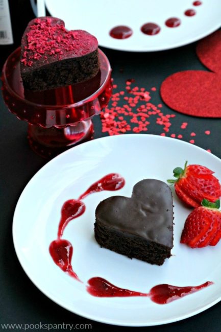 A stunning dark chocolate cake in the shape of a heart with red wine ganache swirled on a white plate.
