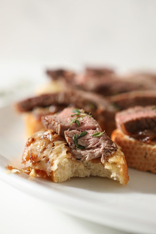 Crispy bites of toast with steak and french onion marmalade on a white plate. 
