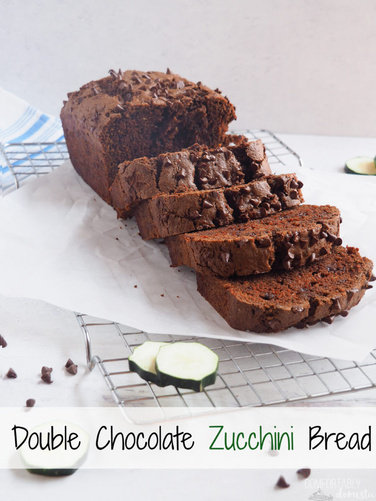 A sliced loaf of double chocolate zucchini bread  resting on parchment paper while cooling on a rack.. 