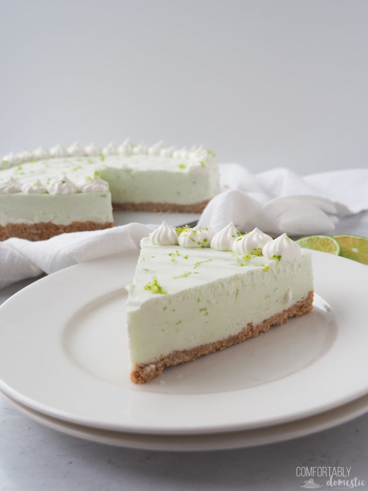 A thick slick of no bake key lime cheesecake on a white plate with the rest of the cheesecake in the background.